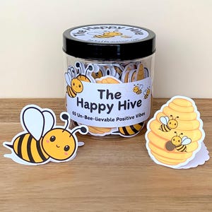 May include: A clear jar with a black lid labeled "The Happy Hive" contains bee-themed stickers. Two bee stickers and a honeycomb sticker are next to the jar. The stickers have yellow and black stripes and the text "60 Un-Bee-lievable Positive Vibes".