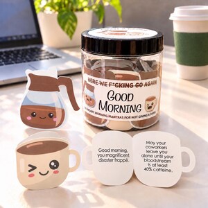 以下が含まれることがあります： 黒い蓋が付いた透明なプラスチック製の瓶で、コーヒーポットやマグカップの形をした紙のカードが入っています。ラベルには「Here we f*cking go again, Good Morning, 36 sweary morning mantras for not giving a damn」と書かれています。開いたカードには同僚とカフェインに関するテキストが表示されています。