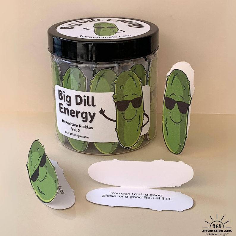 Może przedstawiać: Przezroczysty plastikowy słoik z czarną pokrywką, wypełniony zielonymi kartami w kształcie og&oacute;rk&oacute;w. Słoik jest oznaczony jako "Big Dill Energy" i "30 Positive Pickles Vol 2". Kilka kart w kształcie og&oacute;rk&oacute;w jest rozrzuconych wok&oacute;ł słoika.