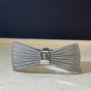 May include: A silver mesh bracelet with a bow design and a silver clasp.