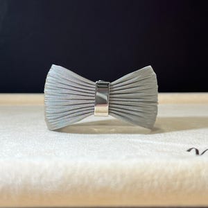 May include: A silver metal bracelet with a bow design. The bracelet is made of a woven metal mesh.