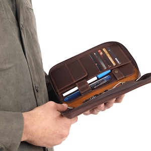May include: A brown leather zippered wallet with multiple card slots, pen holders, and a key chain. The wallet is open and the interior is visible.