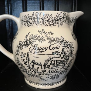May include: White ceramic pitcher with a black and white design of a cow and flowers. The pitcher says "Happy Cow Sweet Milk" on the front.