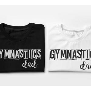 May include: A black t-shirt and a white t-shirt, each featuring the word GYMNASTICS in a block-letter style font with the word dad written in a cursive script underneath. The text on the black shirt is white, and the text on the white shirt is black.