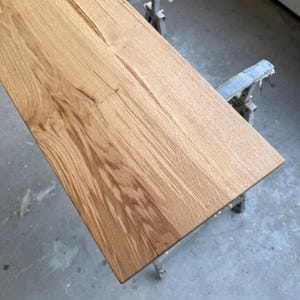 Könnte beinhalten: Ein rechteckiger, unfertiger Holztisch mit natürlicher Maserung. Die hellbraune Oberfläche weist einen diagonal verlaufenden Riss auf. Der Tisch wird von Metallböcken getragen, was auf ein Holzbearbeitungsprojekt hindeutet. Maße: ca. 120 cm x 60 cm.