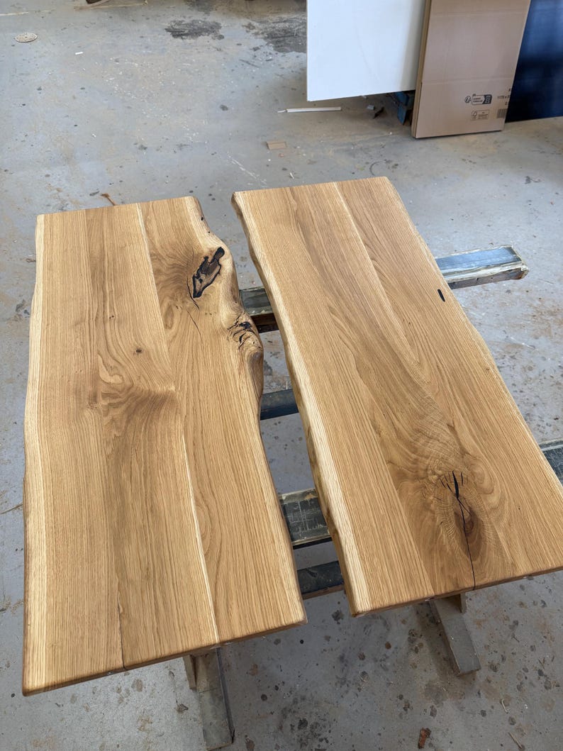 May include: Two rectangular light brown wooden boards with natural live edges. The wood features visible grain patterns, knots, and dark organic markings. The surfaces are smooth and flat, showcasing the raw texture and light tan color of the timber.