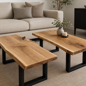 May include: A set of two rectangular coffee tables featuring natural live edge wood tops with visible grain patterns and knots, supported by sturdy black metal U-shaped legs. The tables are positioned side by side, showcasing a light brown wood finish.
