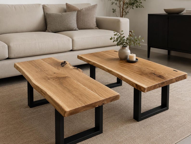 May include: A set of two rectangular coffee tables featuring natural live edge wood tops with visible grain patterns and knots, supported by sturdy black metal U-shaped legs. The tables are positioned side by side, showcasing a light brown wood finish.