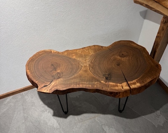May include: A live edge coffee table made from a single piece of wood. The table has a natural, organic shape with visible wood grain and is supported by black metal hairpin legs. The table is approximately 40 inches long.
