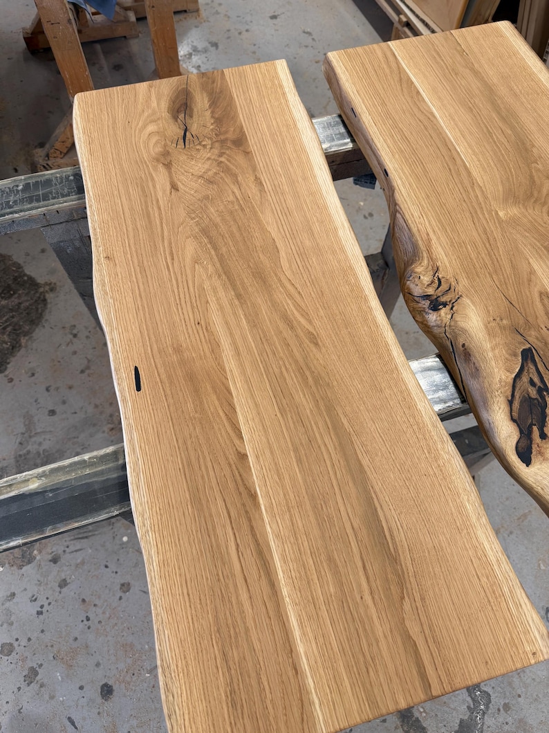 May include: Two rectangular light brown wooden boards with natural live edges. The wood grain is visible throughout the surface, featuring dark knots and organic imperfections that highlight the natural texture of the timber planks.