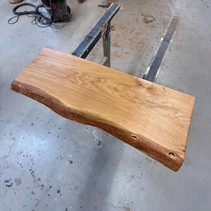 Puede incluir: Una losa de madera rectangular sin terminar con un borde natural. La madera es de color marrón claro con bordes marrón oscuro y veta visible. La losa mide aproximadamente 122 cm de largo y 46 cm de ancho.