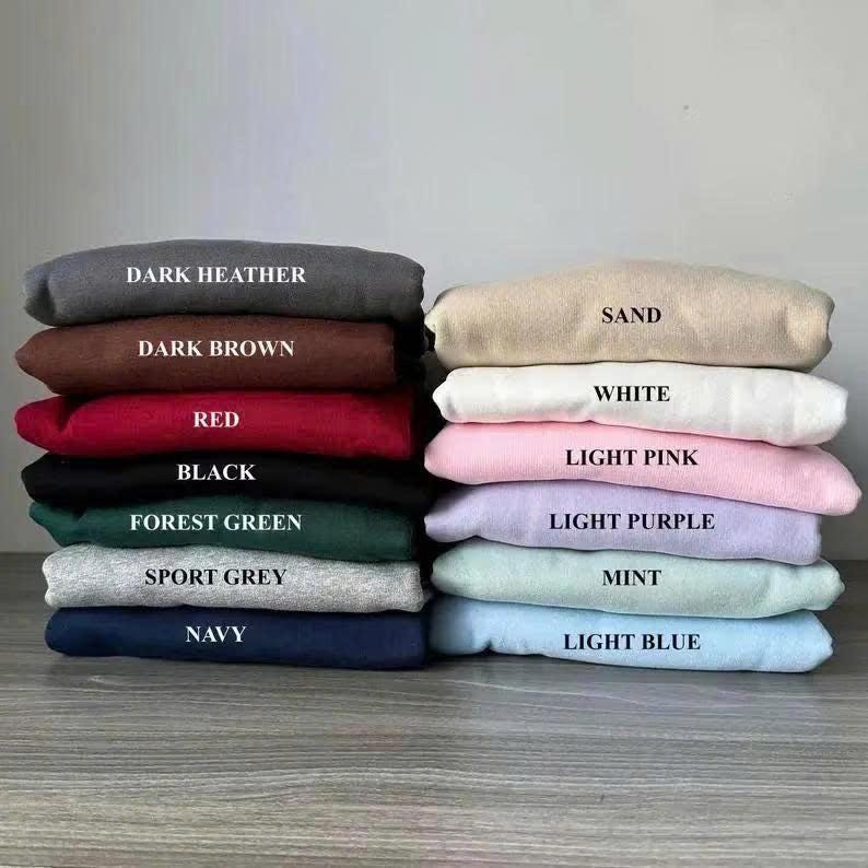 Pu&ograve; includere: Una pila di felpe piegate in vari colori: grigio scuro, marrone scuro, rosso, nero, verde foresta, grigio sportivo, blu navy, sabbia, bianco, rosa chiaro, lilla chiaro, menta e azzurro. Ogni felpa ha un'etichetta con il nome del colore.