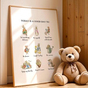 Könnte beinhalten: Ein gerahmter Druck mit dem Text "TODAY IS A GOOD DAY TO" und Illustrationen von Kaninchen und anderen Tieren. Ein großer Teddybär mit brauner Schleife sitzt neben dem Druck. Der Druck hat einen hellen Holzrahmen.