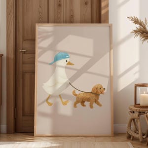 May include: A framed print featuring an illustrated duck wearing a blue baseball cap, walking a small, fluffy brown dog on a leash. The background is a soft, neutral color, and the frame is a light wood.
