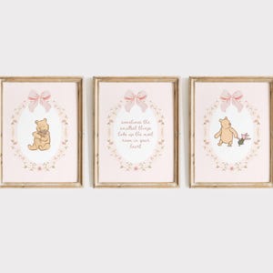 May include: A set of three framed prints with Winnie the Pooh illustrations. Each print has a pink background, floral wreath, and a pink bow. One print shows Pooh hugging a flower, another has text, and the third shows Pooh with Piglet.
