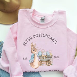 May include: Pink sweatshirt with a graphic of a bunny rabbit pulling a wagon full of Easter eggs. The text reads "Peter Cottontail's Est 1902 Easter Egg Farm".