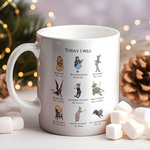 May include: White ceramic mug with a handle, featuring illustrations of characters and the text "TODAY I WILL." The mug has images of a lion, Dorothy, the Tin Man, and other characters from The Wizard of Oz. Marshmallows are scattered around the mug.