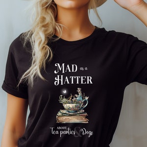 May include: Black t-shirt with a white graphic design featuring a teacup with a Mad Hatter character, a butterfly, and the text "MAD as a HATTER ABOUT Tea parties & Dogs".
