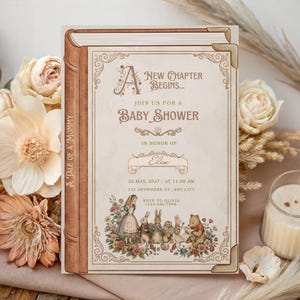 May include: A rectangular baby shower invitation designed to look like an open book with a brown spine and gold corner accents. The text reads A New Chapter Begins, Join Us For A Baby Shower, in honor of Elise, with date, time, and location details.