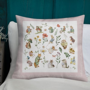 Può includere: Un cuscino da lancio rosa con uno sfondo bianco che presenta un motivo fantasioso di creature del bosco, fiori e piante. Il design include uno scoiattolo, un coniglio, un gufo, un gatto, una volpe, un topo e un'anatra.