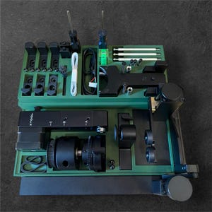 Pode incluir: Uma caixa de ferramentas verde com ferramentas e acessórios pretos. A caixa tem uma etiqueta que diz "XTOOL" no lado. As ferramentas incluem um pequeno motor, uma engrenagem, uma correia e uma variedade de parafusos e outras peças pequenas.