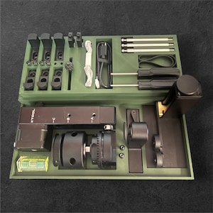 Op de afbeelding: Een groene gereedschapskist met een verscheidenheid aan gereedschappen en accessoires. De kist is open en de gereedschappen zijn zichtbaar. De gereedschappen omvatten een waterpas, een schroevendraaier, een moersleutel en een verscheidenheid aan andere gereedschappen. De kist bevat ook een kleine motor en een set schroeven.