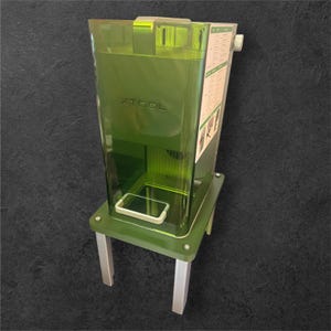 May include: A transparent green machine with the word "XTOOL" printed on the front. The machine has a rectangular base with silver legs. A white rectangular object is inside the machine. A white label with text is on the side.