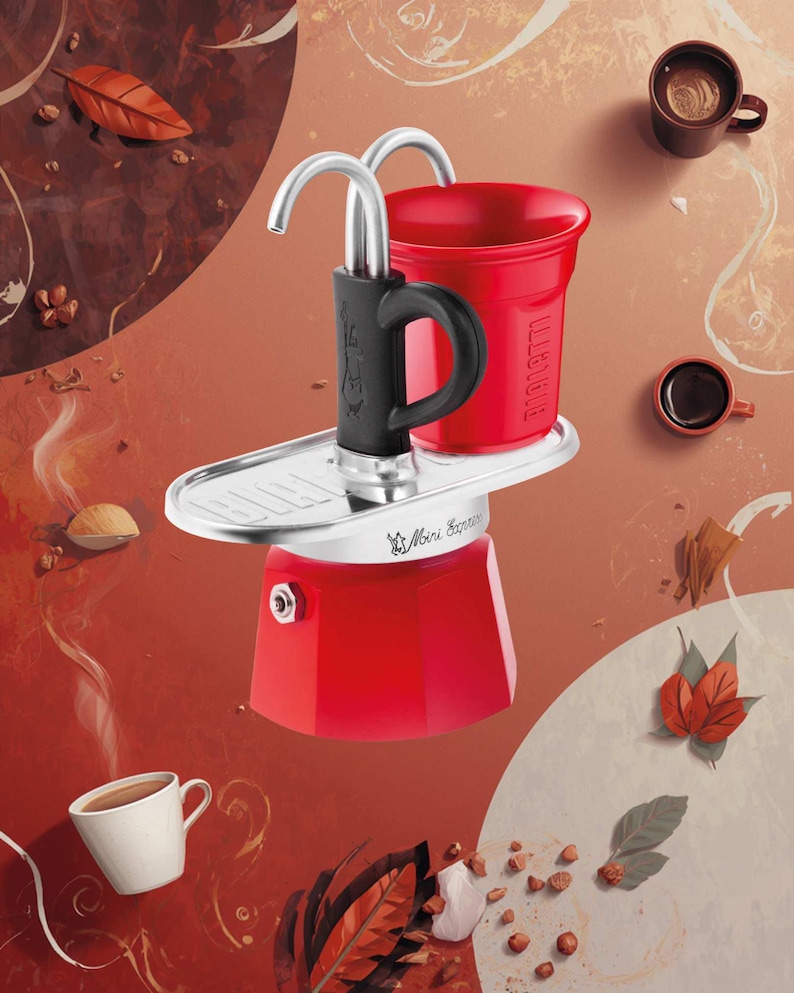 Może przedstawiać: Czerwony ekspres do kawy Mini Express z czarnym uchwytem i srebrnymi akcentami. Obraz zawiera filiżanki kawy, ziarna kawy i jesienne liście na czerwonobrązowym tle. Słowo "BIALETTI" jest widoczne na czerwonym kubku.
