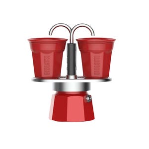 Może przedstawiać: Czerwony ekspres do kawy z dwiema pasującymi czerwonymi filiżankami. Na filiżankach napis "BIALETTI". Ekspres do kawy ma srebrną podstawę i czarny uchwyt. Filiżanki są połączone z podstawą srebrnym łukiem.