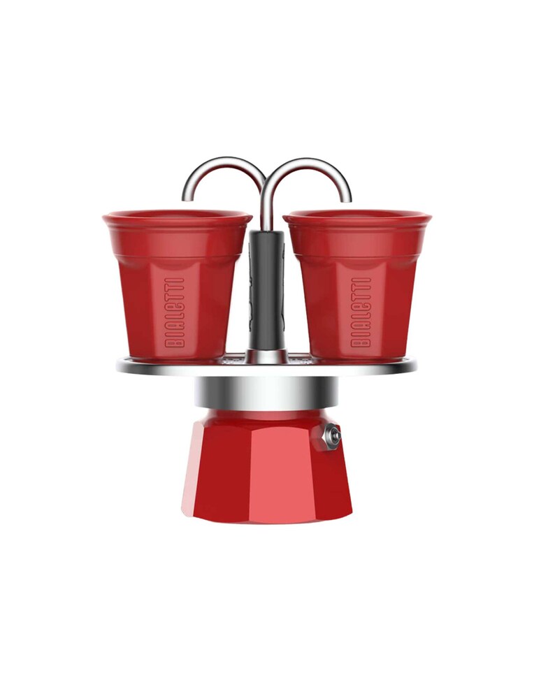 Może przedstawiać: Czerwony ekspres do kawy z dwiema pasującymi czerwonymi filiżankami. Na filiżankach napis "BIALETTI". Ekspres do kawy ma srebrną podstawę i czarny uchwyt. Filiżanki są połączone z podstawą srebrnym łukiem.