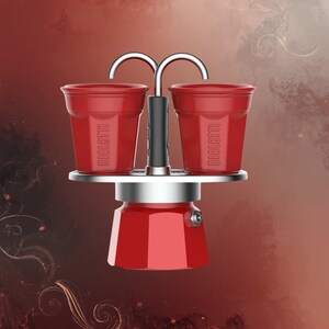 Może przedstawiać: Czerwony ekspres do kawy Bialetti z dwoma pasującymi czerwonymi filiżankami. Filiżanki są umieszczone nad ekspresem do kawy, połączone srebrnym uchwytem. Ekspres do kawy ma srebrną podstawę i czerwony korpus. Tło to gradient czerwieni i brązu.