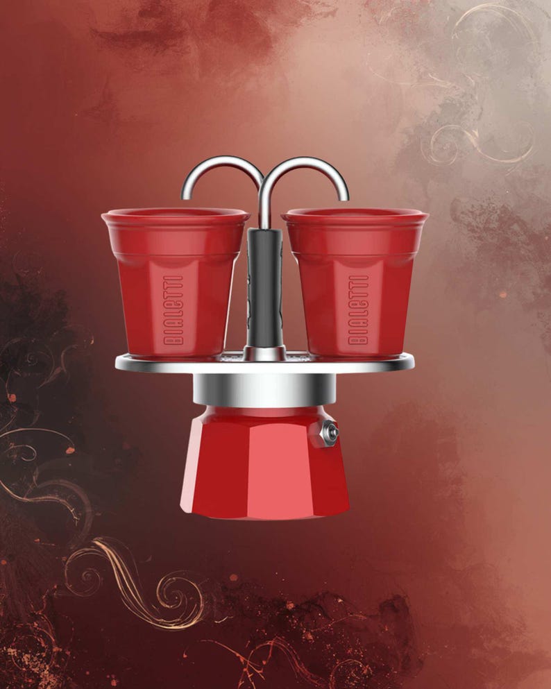 Może przedstawiać: Czerwony ekspres do kawy Bialetti z dwoma pasującymi czerwonymi filiżankami. Filiżanki są umieszczone nad ekspresem do kawy, połączone srebrnym uchwytem. Ekspres do kawy ma srebrną podstawę i czerwony korpus. Tło to gradient czerwieni i brązu.