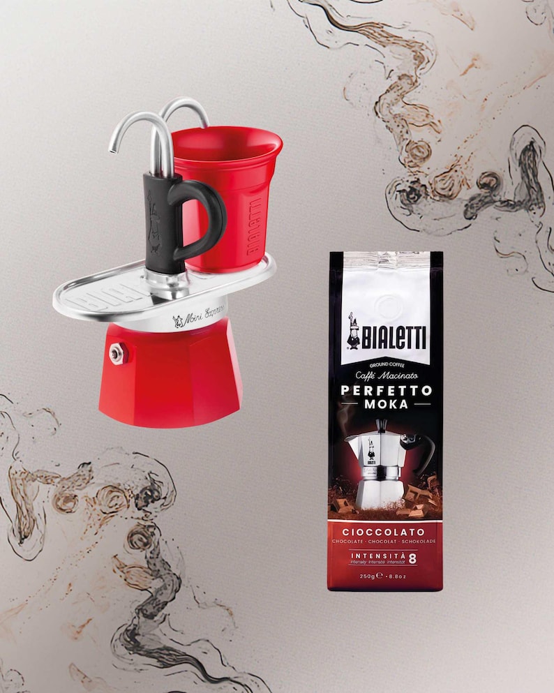 Może przedstawiać: Czerwony ekspres do kawy Bialetti Moka z czarnym uchwytem i czerwoną filiżanką. Na zdjęciu znajduje się r&oacute;wnież torebka mielonej kawy Bialetti z napisem "PERFETTO MOKA". Torebka kawy jest ciemnoczerwona i czarna z napisem "CIOCCOLATO" i "INTENSIT&Agrave; 8".