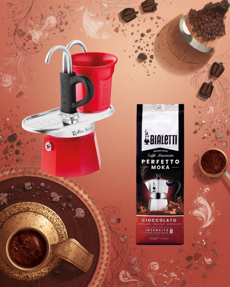 Może przedstawiać: Czerwony ekspres do kawy Bialetti z czarnym uchwytem i czerwonym kubkiem. Obok ekspresu znajduje się paczka kawy mielonej Bialetti z napisem "Perfetto Moka Cioccolato". Na zdjęciu znajduje się r&oacute;wnież czekolada i ziarna kawy.