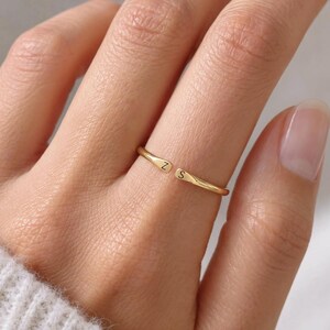 May include: A thin, gold-coloured open ring featuring two flat, tapered ends. Each end is engraved with a single uppercase letter, specifically the letter Z on one side and the letter S on the other, creating a minimalist and adjustable band design.