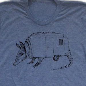 May include: A blue t-shirt with a black and white illustration of an armadillo pulling a camper.