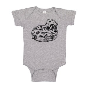 May include: A gray baby bodysuit with a black and white illustration of a pizza. The pizza is sliced into several pieces, with one slice lifted to reveal the word "CHICAGO". The bodysuit has short sleeves and snap closures.