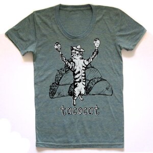 May include: A teal blue t-shirt with a graphic of a cat wearing a sombrero and holding maracas. The cat is standing on a pile of tacos. The text "tacocat" is printed below the cat.
