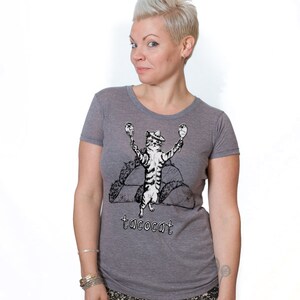 May include: A heather grey t-shirt with a black and white illustration of a cat wearing a sombrero and holding maracas. The cat is standing on top of two tacos. The text "tacocat" is printed below the cat.