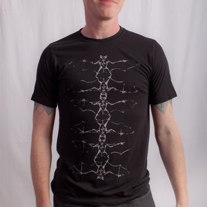 May include: A black t-shirt with a white graphic design of a stylized spine. The design is centered on the shirt and extends from the neck to the bottom hem.