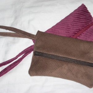 May include: A brown corduroy zippered pouch with a pink corduroy handle. The pouch has a zipper closure and a brown zipper pull.