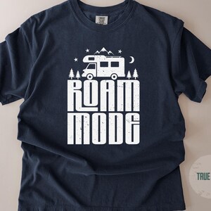May include: A true navy short-sleeve t-shirt featuring a white graphic print of a camper van, mountains, trees, stars, and a crescent moon. The text ROAM MODE is printed in a bold, distressed white font centered below the camper van illustration.