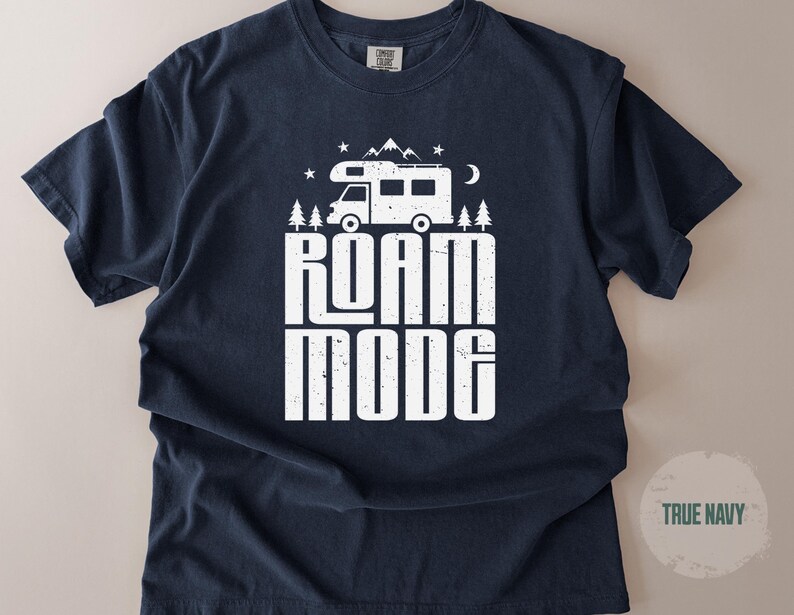 May include: A true navy short-sleeve t-shirt featuring a white graphic print of a camper van, mountains, trees, stars, and a crescent moon. The text ROAM MODE is printed in a bold, distressed white font centered below the camper van illustration.