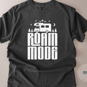 May include: A charcoal gray short-sleeve t-shirt featuring a white graphic print of a camper van, pine trees, mountains, stars, and a crescent moon. The text ROAM MODE is printed in large, distressed white capital letters below the camper van.