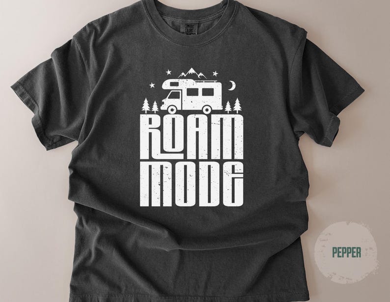 May include: A charcoal gray short-sleeve t-shirt featuring a white graphic print of a camper van, pine trees, mountains, stars, and a crescent moon. The text ROAM MODE is printed in large, distressed white capital letters below the camper van.