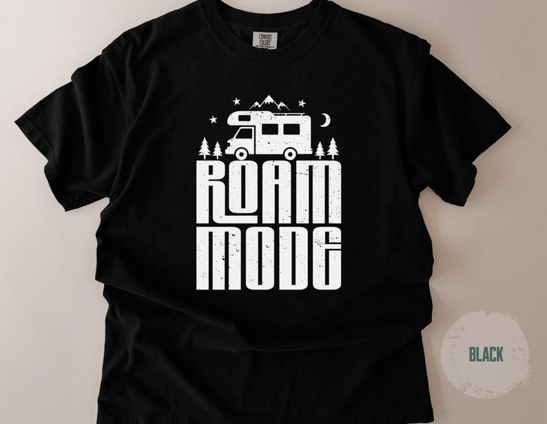 May include: A black short-sleeve t-shirt featuring a white graphic print of a camper van, pine trees, mountains, stars, and a crescent moon. The text ROAM MODE is printed in large, bold, distressed white capital letters below the camper van graphic.