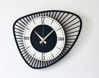 Può includere: Un orologio bianco e nero con un design unico a forma di raggio di sole. Il quadrante dell'orologio è bianco con numeri e lancette neri. L'orologio è montato su una parete bianca.