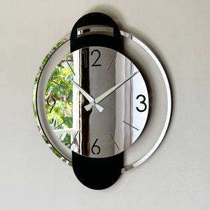 May include: A modern silver and black wall clock with a mirrored face and a black outer ring. The clock has a simple design with black numbers and hands.