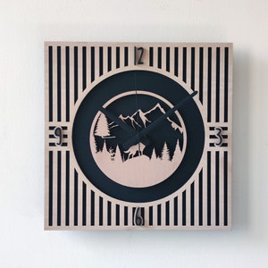 Puede incluir: Un reloj cuadrado de madera con rayas blancas y negras. La esfera del reloj es un círculo negro con una escena de montaña y una aguja de reloj negra. Los números 12, 3, 6 y 9 son visibles en la esfera del reloj.