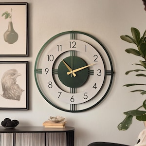 May include: A contemporary wall clock with a green frame and a white face. The clock has gold hands and black numerals. The clock's design is minimalist and elegant, suitable for home decor. The clock measures approximately 46 cm in diameter.